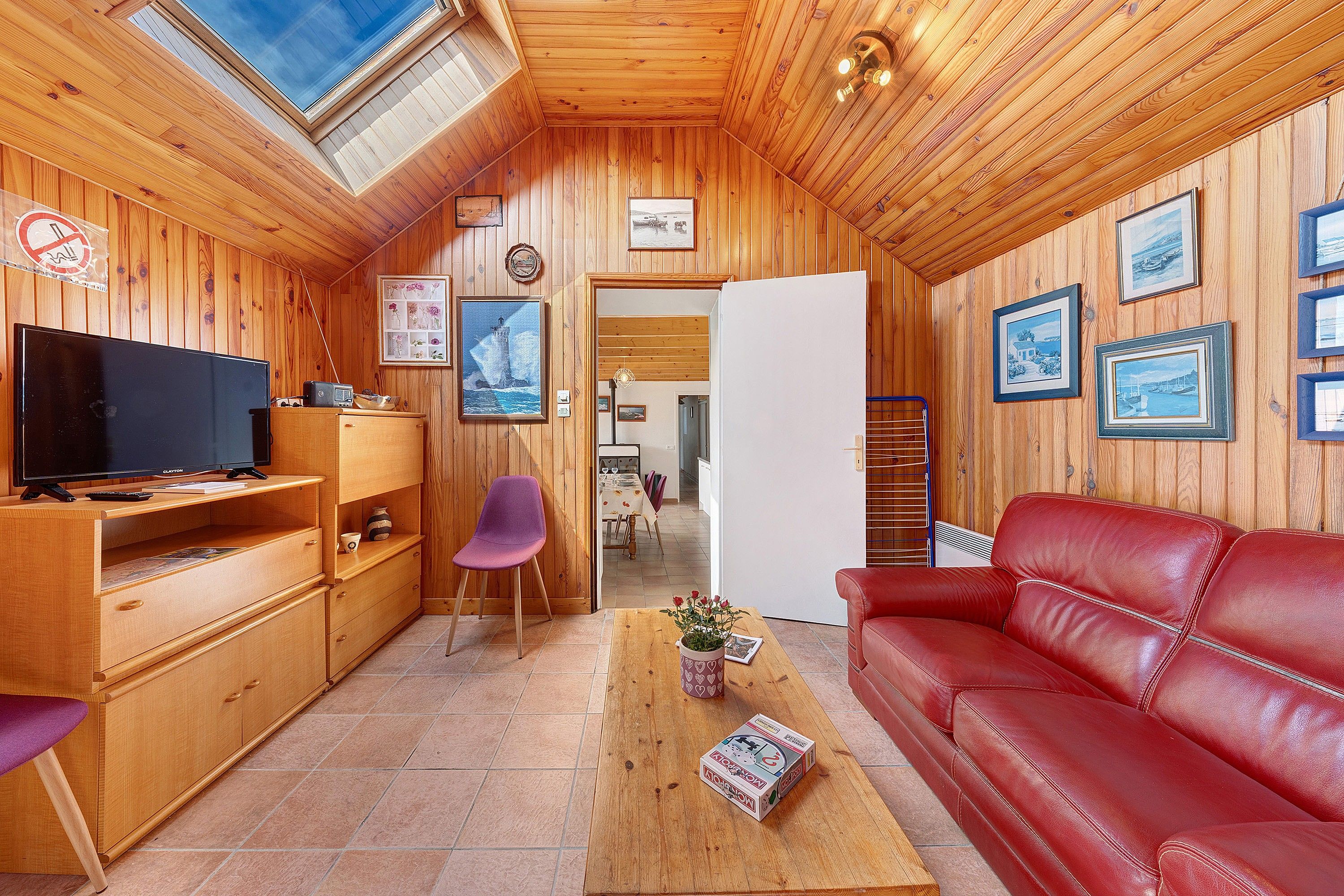 Ein gemütliches Holzinterieur mit Fernseher, einer roten Ledersofa und gerahmten Bildern an den Wänden.