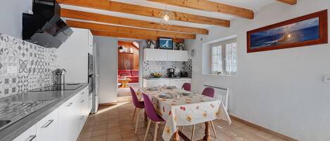 A modern kitchen with wooden beams, a dining area with a table set for four, and a kitchen island with a sink and stove.