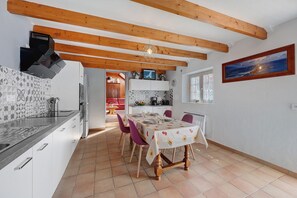 A modern kitchen with wooden beams, a dining area with a table set for four, and a kitchen island with a sink and stove.