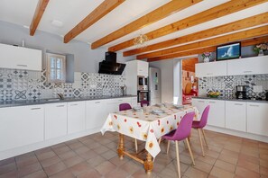 A modern kitchen with white cabinetry, a dining table set for four, and a tiled backsplash.