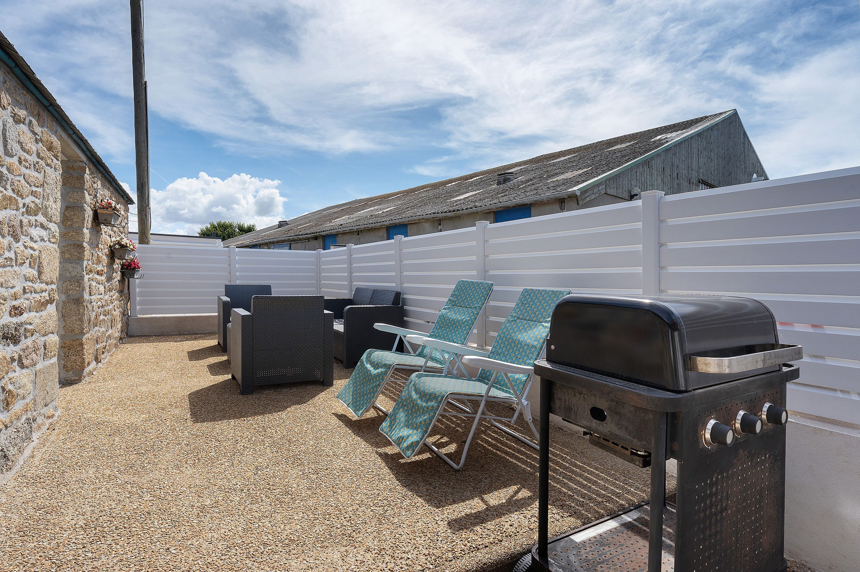 An outdoor patio with a barbecue grill, lounge chairs, and a stone wall.