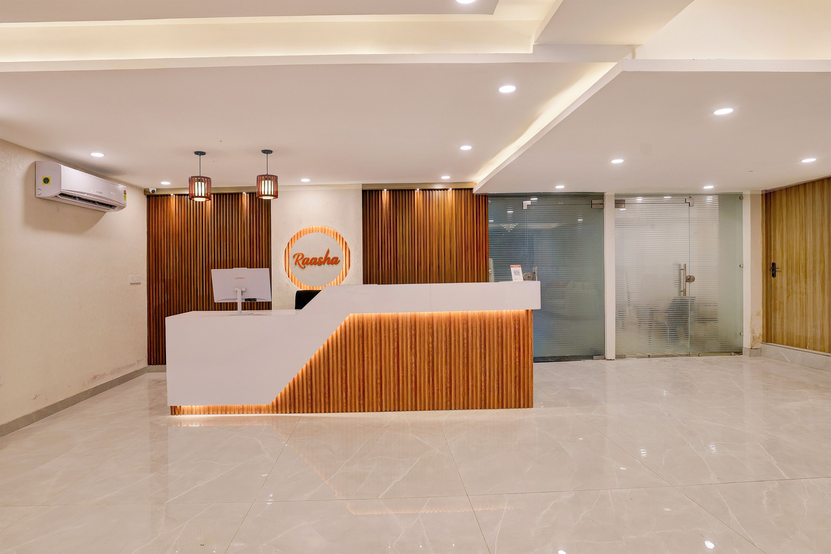 A modern reception desk with a logo, a white air conditioning unit, and a glass door entrance.