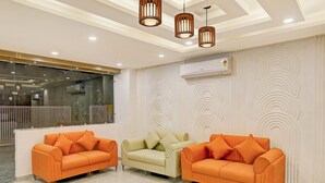 Un área de recepción con tres sofás, uno naranja y dos color crema, con un diseño moderno en el techo y una unidad de aire acondicionado en la pared.
