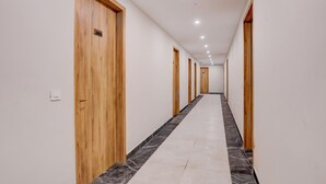Un pasillo largo y estrecho con puertas de madera en un lado y suelo de baldosas.