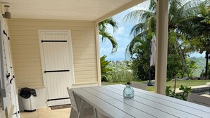 A covered patio with a white table and chairs, a door, and a view of the ocean and greenery. - A small, contemporary home, perfect for families: Villa Nathoun's. (Rivière-Salée)