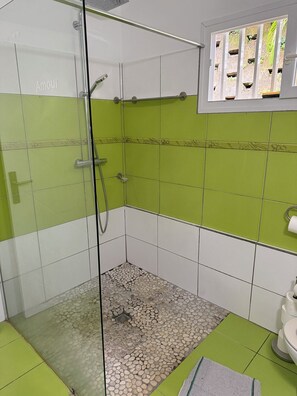 A shower area with green and white tiles, a glass door, and a small window with a view of greenery. - A small, modern home, perfect for families: Villa Nathoun's. (Rivière-Salée)