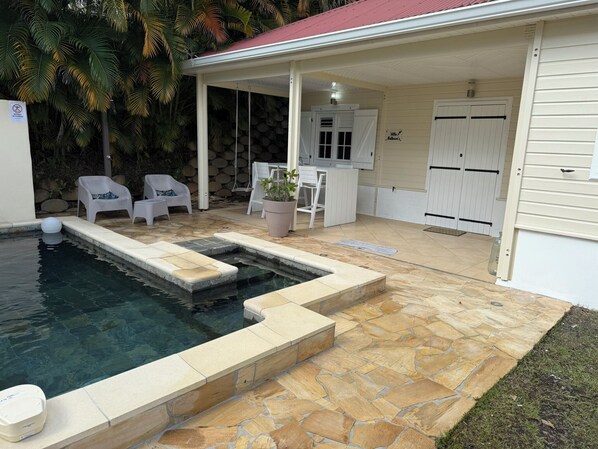 A pool area with stone steps leading into the water, a covered seating area with chairs, and a white building with a sign reading "Villa". - A small, modern home, perfect for families: Villa Nathoun's. (Rivière-Salée)