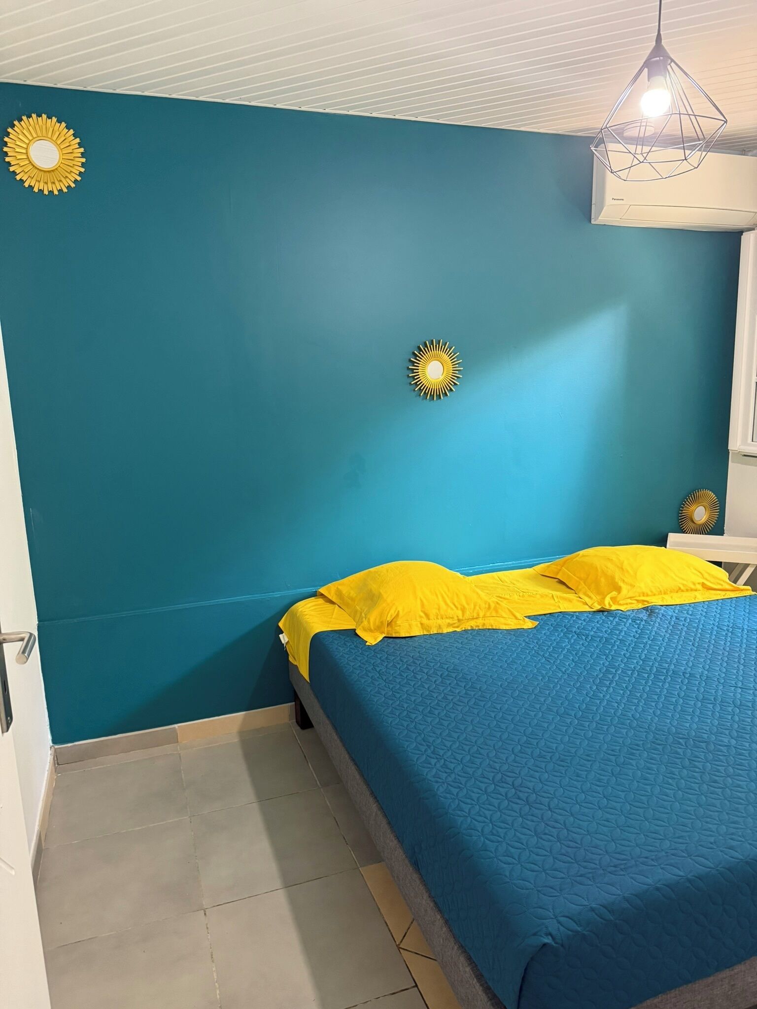 Ein Zimmer mit Türkiswänden, einem Bett mit blauer Bettwäsche und zwei Wandleuchten.