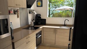 A modern kitchen with light wood cabinets, a black countertop, a built-in oven, and a window with a view of greenery. - A small, contemporary home, perfect for families: Villa Nathoun's. (Rivière-Salée)