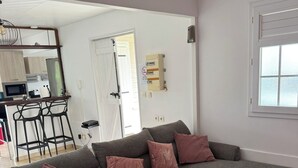 A grey sectional sofa with four cushions, a kitchen area with a microwave and a coffee maker, and a window with blinds. - A small, contemporary home, perfect for families: Villa Nathoun's. (Rivière-Salée)