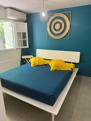 A bedroom with a white bed, blue bedding, and a decorative wall piece. - A small, modern home, perfect for families: Villa Nathoun's. (Rivière-Salée)