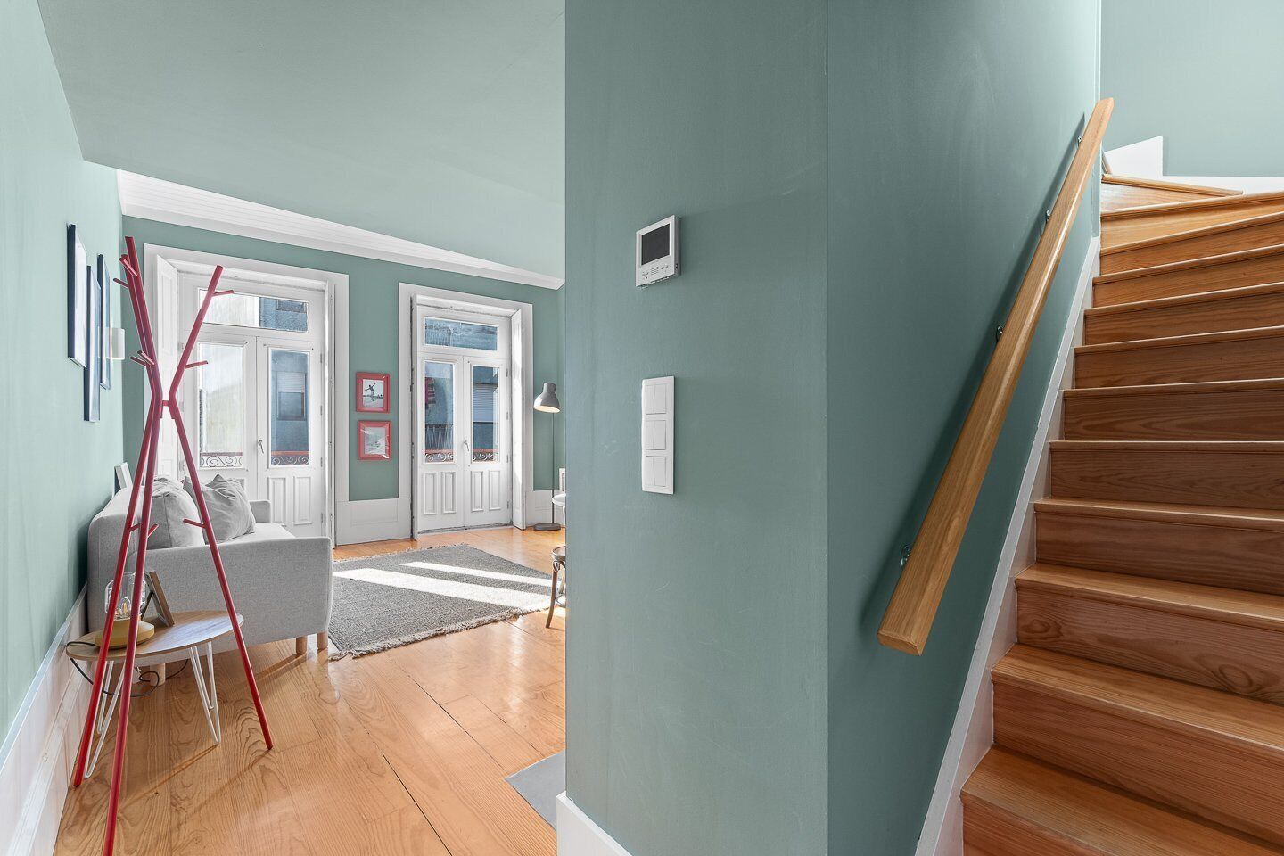 Un pasillo con una escalera de madera, una escalera roja y una puerta que da a otra habitación.