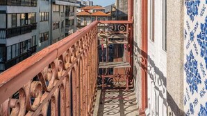 Ein schmaler Balkon mit aufwendig gestalteten Metallgeländern, einer Wand mit blauen Blumenmustern und Blick auf angrenzende Gebäude.