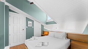 Ein Schlafzimmer mit Bett, Nachttisch, Wandleuchte, einem gerahmten Bild und einer Tür.