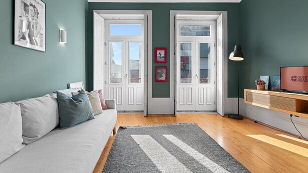 Ein modernes Wohnzimmer mit einem grauen Sofa, einem grau-weißen Teppich, Holzboden, einem Fernseher auf einem Holzschrank und zwei Glastüren.