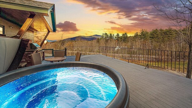 Ein Whirlpool auf einer Holzdielen-Terrasse mit Blick auf einen Sonnenuntergang und Berge.