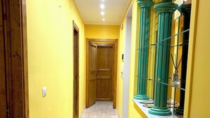 Un pasillo con paredes amarillas, una puerta de madera al final y columnas verdes a la derecha.