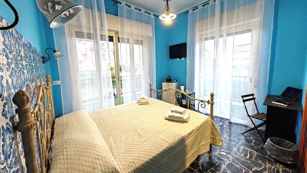 Un dormitorio con cama, escritorio, silla, televisión y vistas al balcón.
