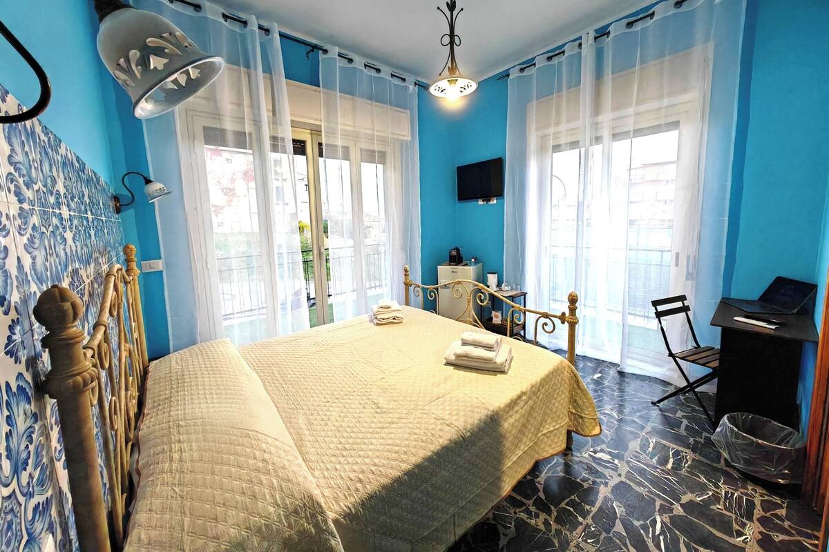 A bedroom with a bed, a desk, a chair, a TV, and a balcony view.