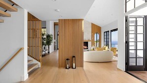 A spacious living area with a wooden floor, a white sofa, and a large window providing a view of the outdoors. - Villa Costera - Tree-lined Tranquility: 3-level Entertainer's Dream (Malibu)