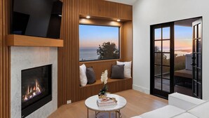 A modern living room with a fireplace, a large window with a view, and a seating area. - Villa Costera - Tree-lined Tranquility: 3-level Entertainer's Dream (Malibu)