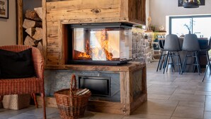 Une cheminée avec une façade en verre, un fauteuil en osier et un coin repas avec des chaises et une table.