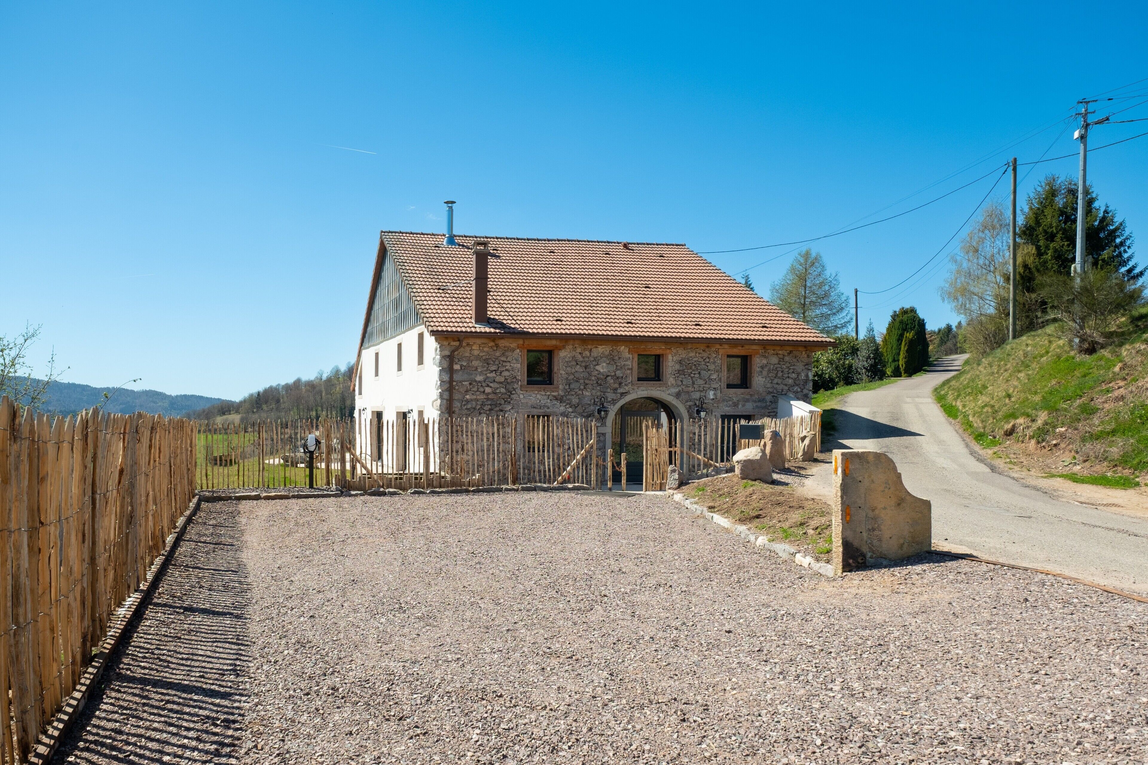 A stone building with a tiled roof, a gravel driveway, and a wooden fence.