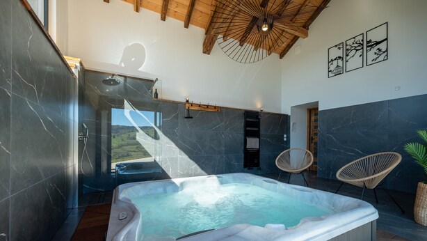 Une salle de bain moderne avec une grande baignoire, des poutres en bois au plafond et une vue sur l’extérieur.