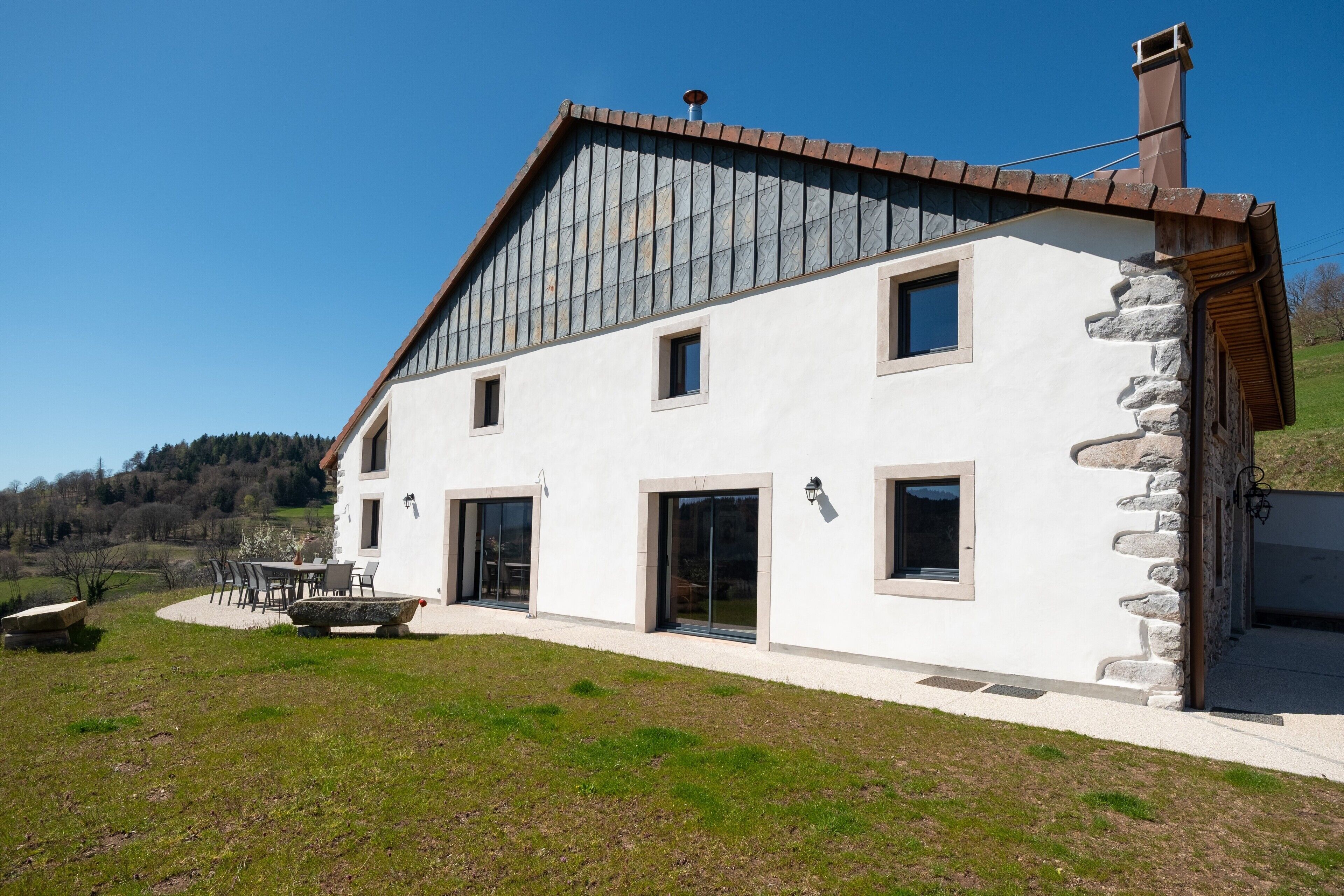 Une maison moderne à deux étages, dotée d’une façade en pierre, de grandes fenêtres et d’un toit en pente.