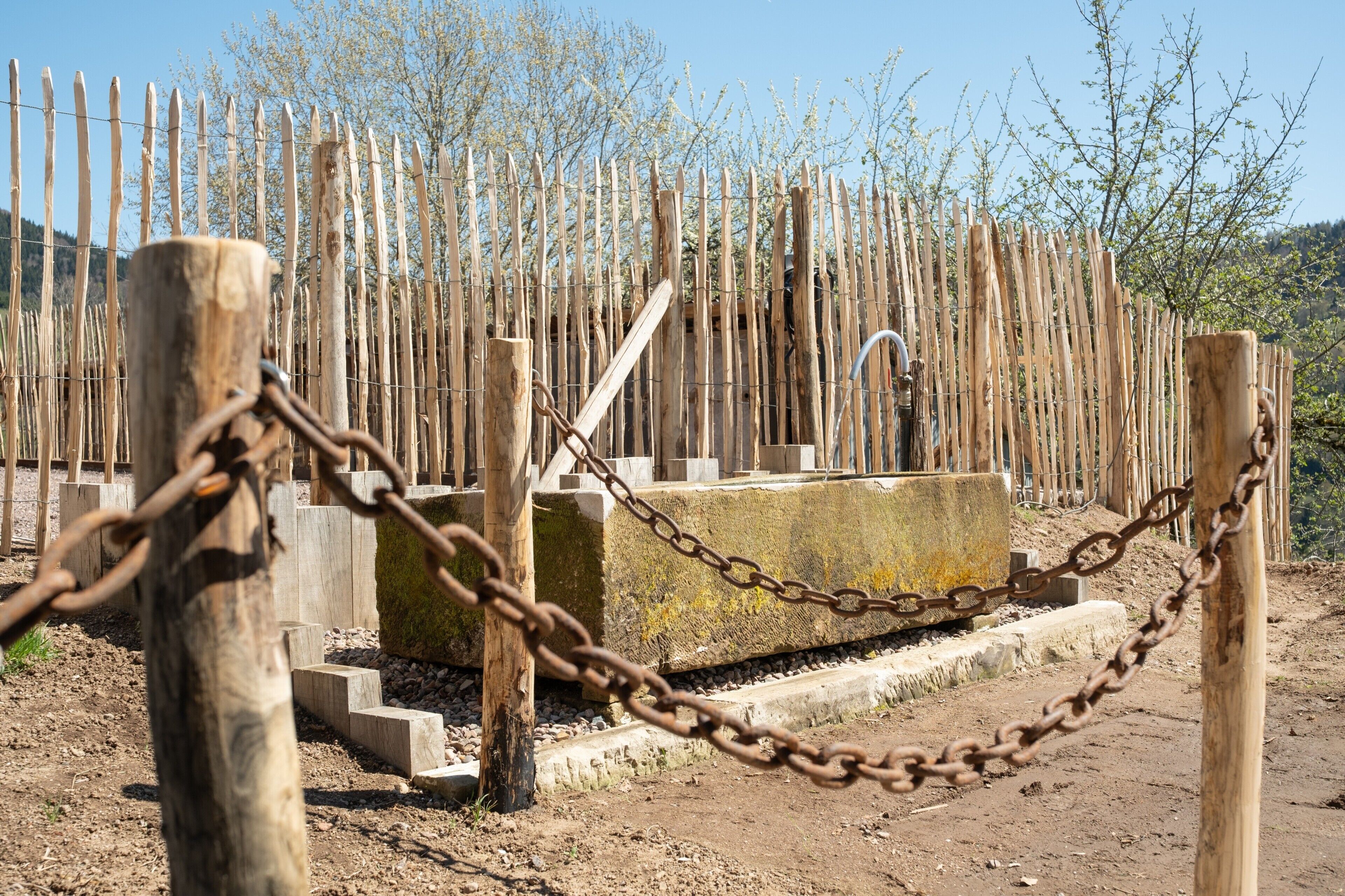 A rustic wooden fence with a chain barrier, a concrete structure, and a person in the background.