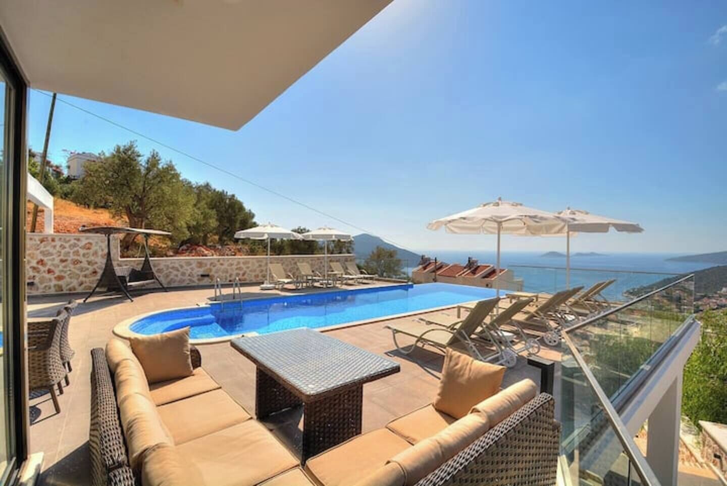 Un espace piscine aménagé sur le toit, avec des chaises longues et des parasols, offrant une vue panoramique sur la mer et les collines.
