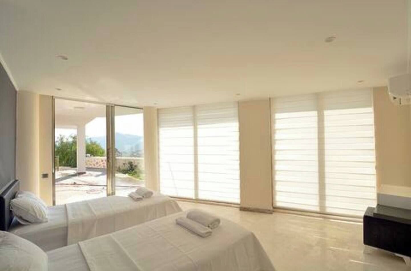 Une chambre d’hôtel moderne avec deux lits, une grande porte-fenêtre coulissante donnant sur un espace extérieur et une vue sur les montagnes.