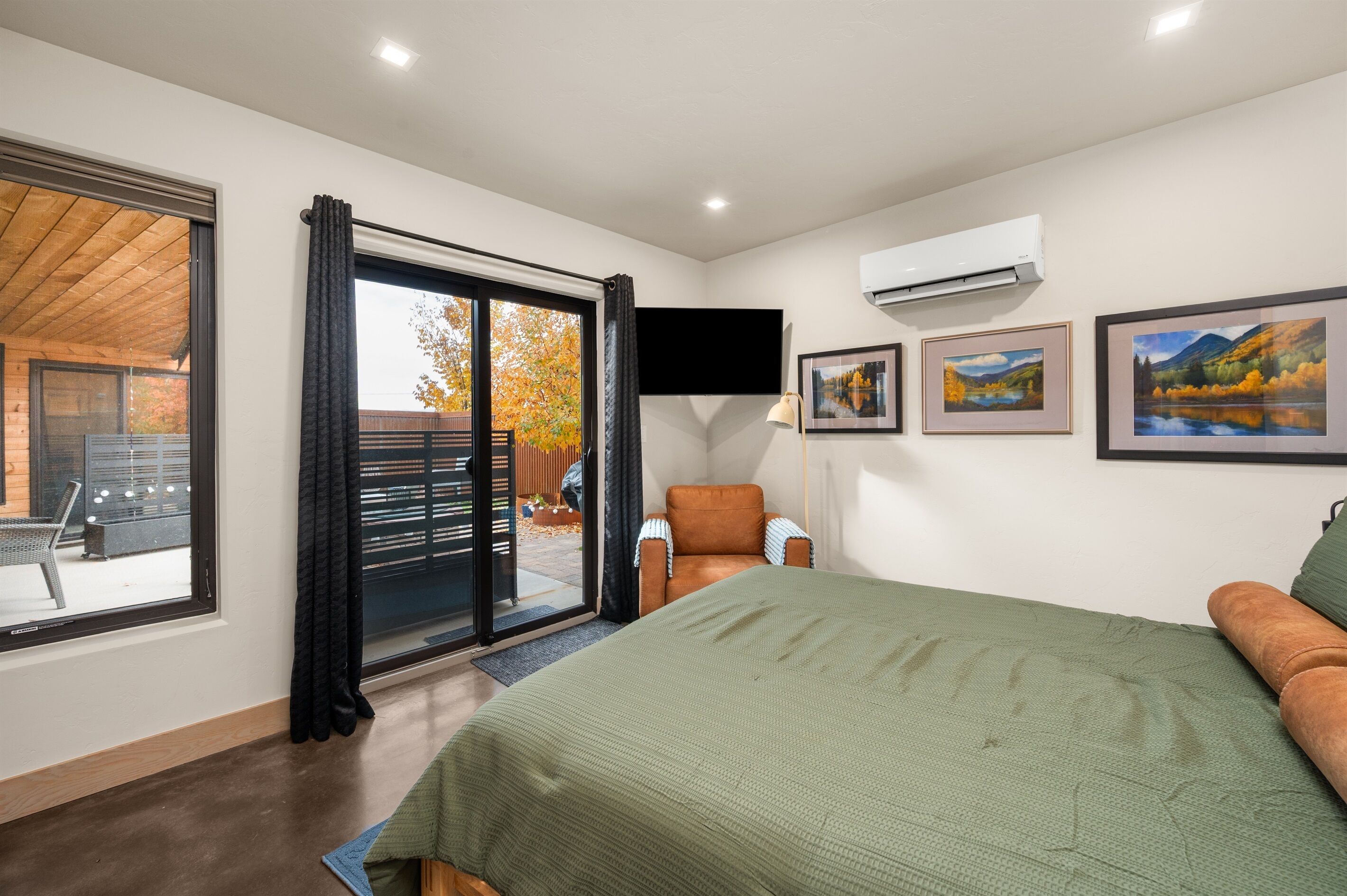 Ein Schlafzimmer mit einem großen Bett, einem Sessel, einem Schreibtisch und einem Fenster mit Vorhängen.