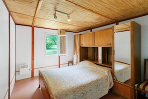 Une chambre avec un plafond en bois, un lit recouvert dâune couvre-lit Ă motifs, une armoire et une fenĂȘtre avec des rideaux.