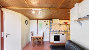 Une pièce avec un plafond en bois, une table à manger avec des chaises, un canapé en cuir noir, un coin cuisine avec une cuisinière et un évier, et une horloge murale.