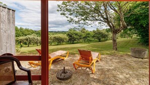 Un espace extérieur aménagé avec des chaises et une table, une structure en bois et une vue sur un paysage verdoyant parsemé d’arbres.