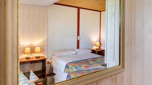 Une chambre avec un plafond en bois, un lit avec une literie blanche, deux lampes de chevet et un miroir au mur.
