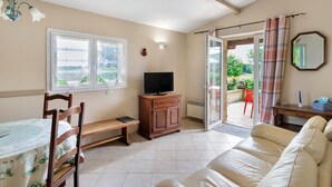 A room with a sofa, a television on a wooden cabinet, a bench, a table with a checkered tablecloth, and a sliding glass door leading to an outdoor area. - Gite Charly: Private Terrace, Shared Garden, Pool & Wi-Fi in Salignac Eyvigues (Salignac Eyvigues)