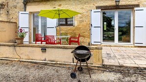 A stone building with a patio, a grill, and outdoor seating. - Gîte Charly: Private Terrace, Shared Garden, Pool & Wi-Fi in Salignac Eyvigues (Salignac Eyvigues)