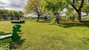 A grassy outdoor area with playground equipment, including a slide and swings, and a green dinosaur toy. - Gîte Charly: Private Terrace, Shared Garden, Pool & Wi-Fi in Salignac Eyvigues (Salignac Eyvigues)