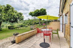 Une terrasse avec des meubles d’extérieur, un barbecue et un parasol jaune.