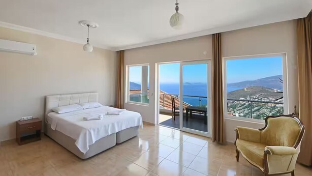 Un'ampia camera d'albergo con un letto grande, una poltrona e un balcone con vista sulla città.