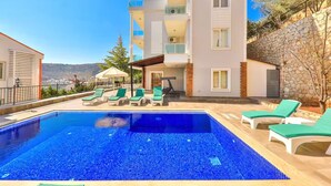 Un edificio moderno a due piani con piscina, poltrone da relax verdi e un muro in pietra.