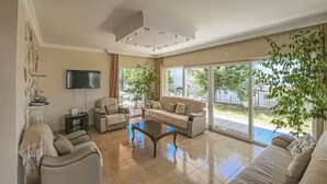 Un soggiorno spazioso con un divano grande, un tavolino e una televisione. Una porta scorrevole in vetro dà accesso a una zona esterna con vista sul verde.