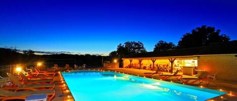 A swimming pool with lounge chairs and a bar area, surrounded by a low wall and trees.