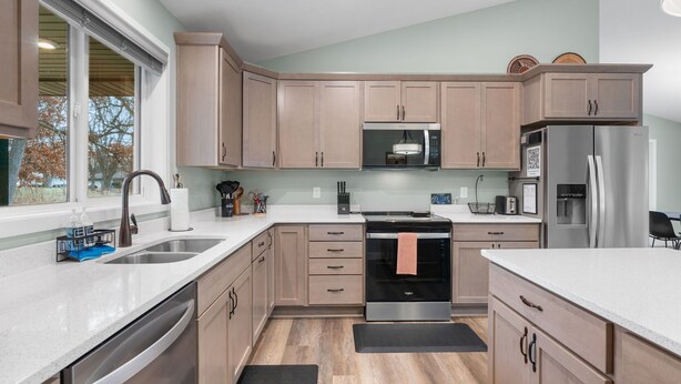 A modern kitchen with light wood cabinets, stainless steel appliances, and a large window providing natural light. - Hansen Park Place (New Brighton)