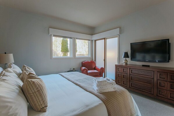 Un dormitorio con una cama grande, un televisor, una silla roja y una ventana.