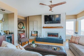 Un salon moderne doté d’une cheminée, d’un ventilateur de plafond et d’un grand téléviseur fixé au mur.