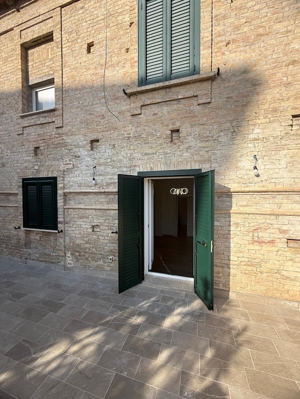 A building with a brick facade, a green door, and a window with shutters.