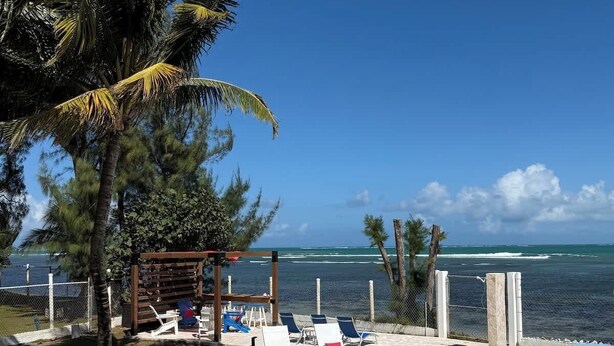 A pool area with lounge chairs, a wooden pergola, and a view of the ocean. - Beachfront, Spacious Home, Private Luxury Pool! (Palmer)
